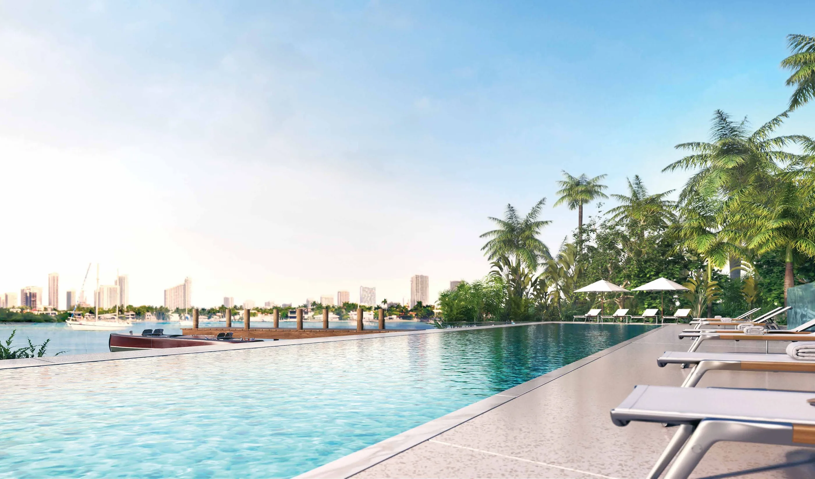 The pool deck along the bay, loungers under palms beside the long pool with the dock beyond